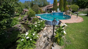 A swimming pool surrounded by a garden with rocks, plants, and a lamp post. - Aldea Os Muiños (Rianxo)