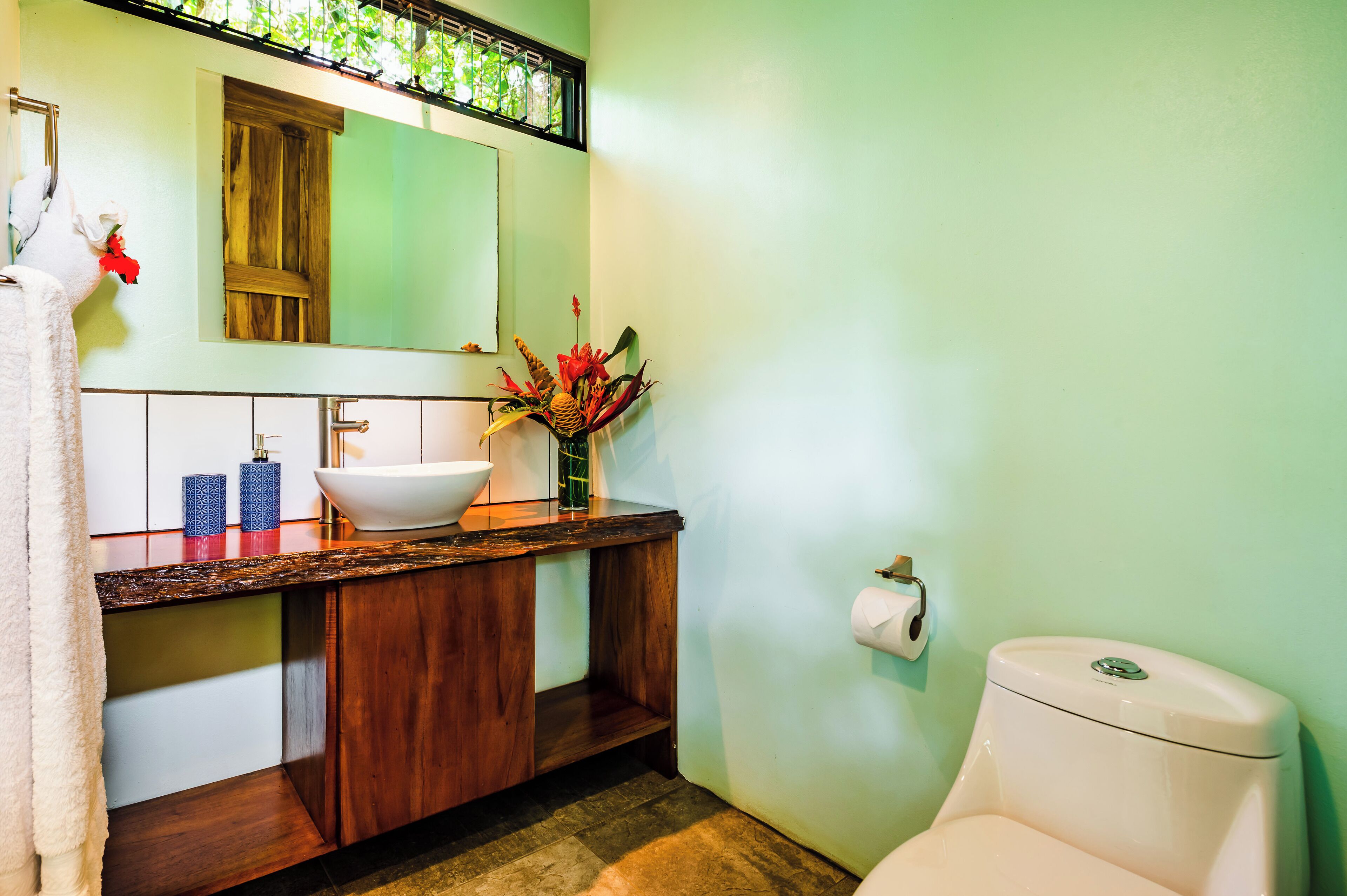Een badkamer met een witte wastafel, een houten opbergmeubel, een spiegel, een toilet en een kleine plant op het aanrecht.
