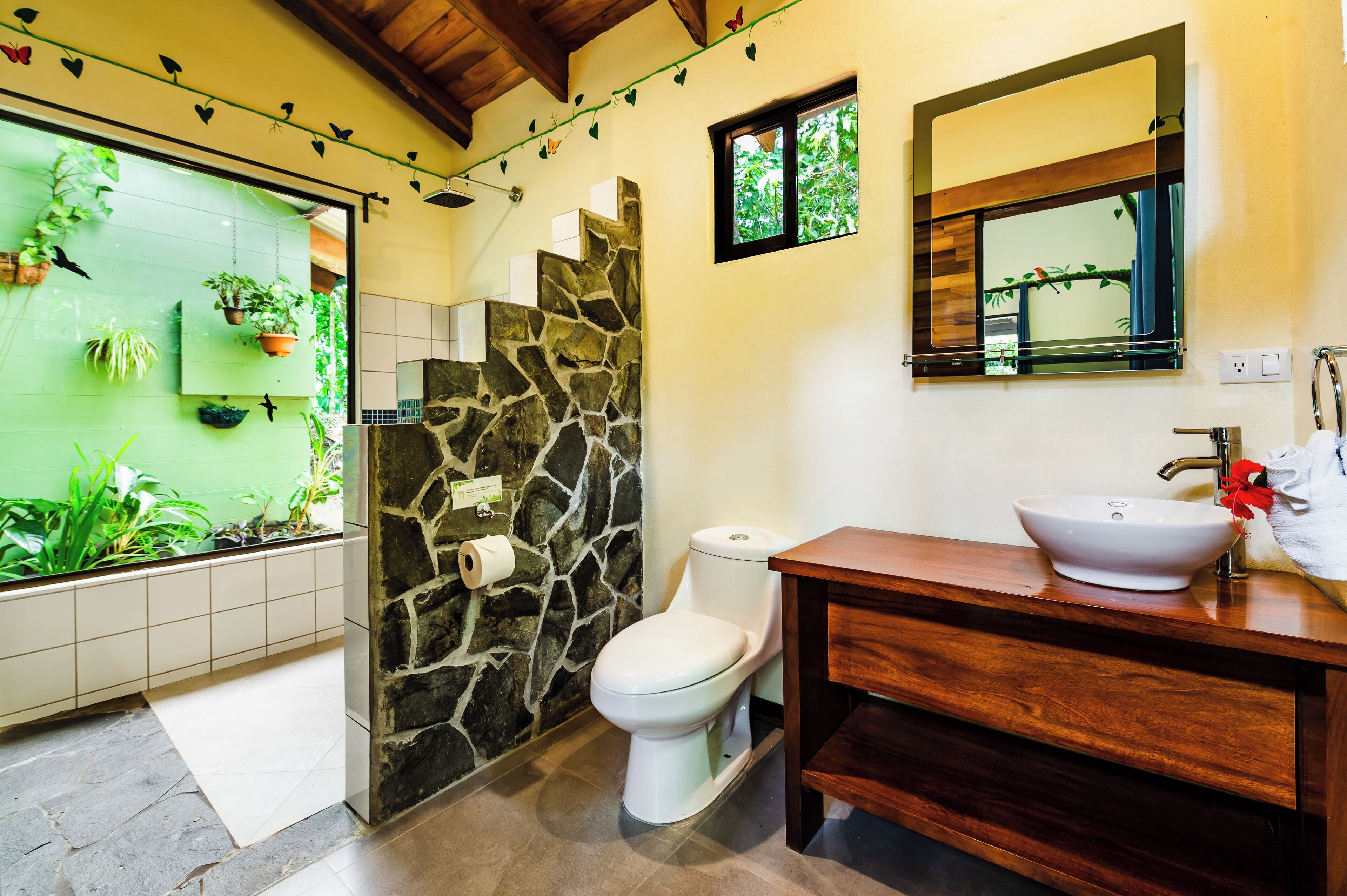A bathroom with a stone wall, a toilet, a sink, and a mirror.