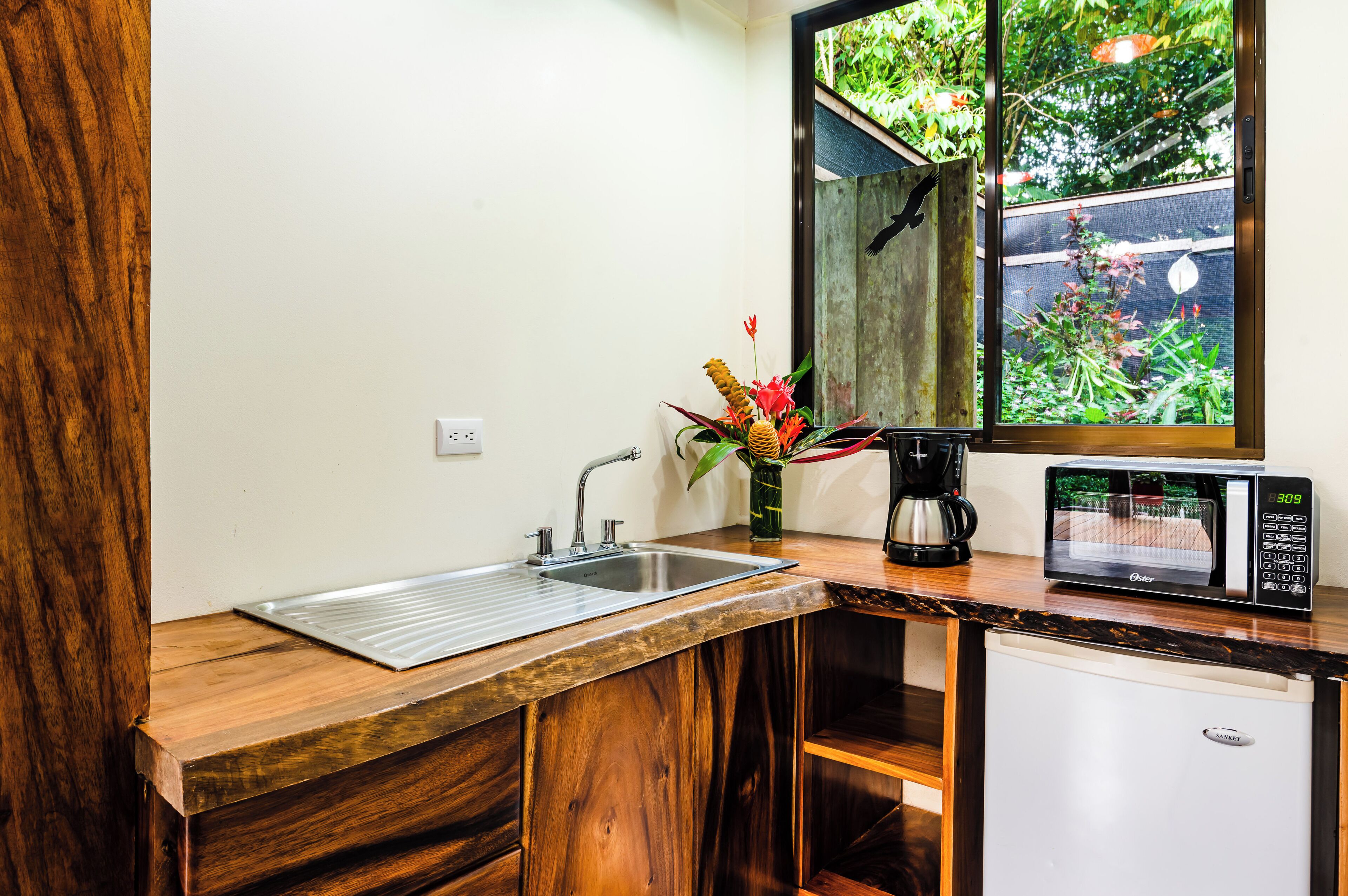 Cocina compacta con lavamanos, cafetera, microondas y refrigerador pequeño.