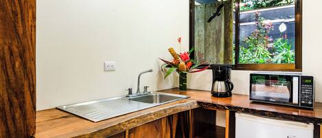 Cocina compacta con lavamanos, cafetera, microondas y refrigerador pequeño.