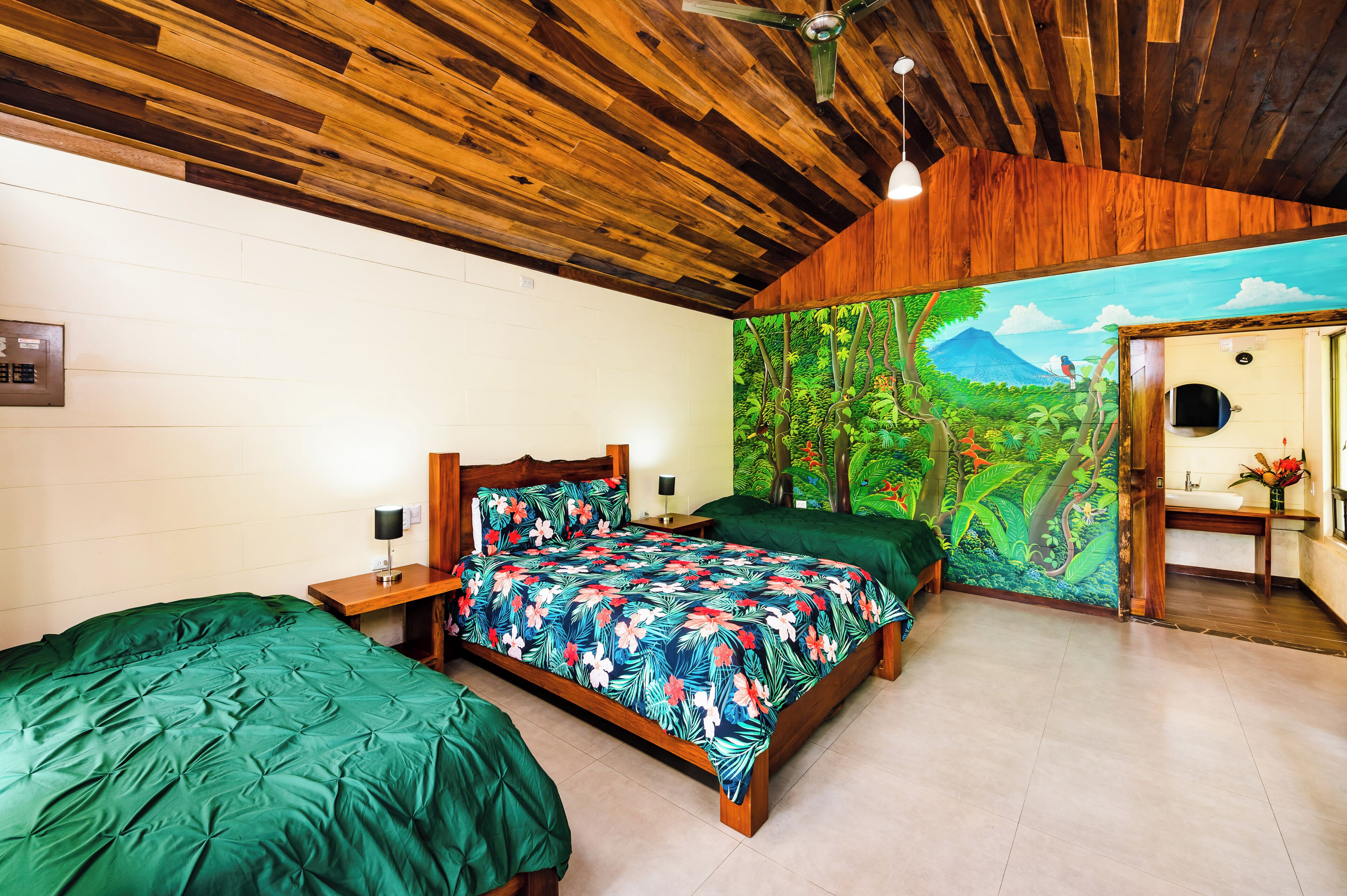 A room with a wooden ceiling, a bed with a floral bedspread, a nightstand, and a wall mural of a jungle scene.