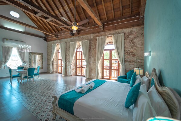 A spacious bedroom with a large bed, a dining area, and a chandelier.