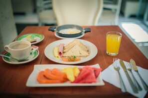 Una tavola imbandita con fette di pane tostato, frutta fresca, una tazza di caffè e un bicchiere di succo d'arancia, oltre a una padella.