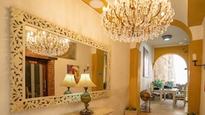 A hallway with a large ornate mirror, a stone bench, a chandelier, and a dining area in the background. - Hotel Casa Tere (Cartagena)