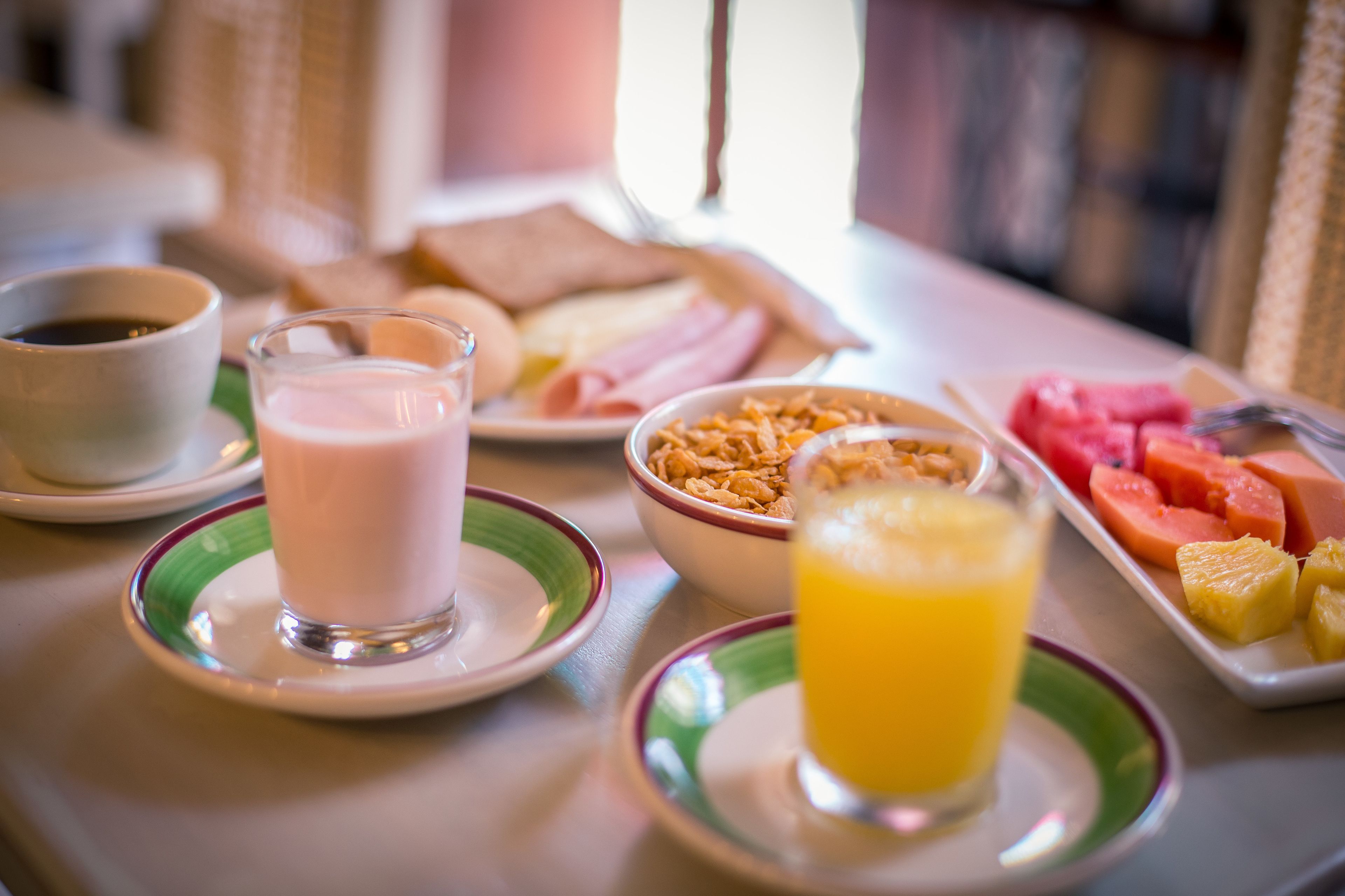 A breakfast table with a cup of coffee, a glass of milk, a bowl of cereal, a plate of fruit, and a glass of orange juice.