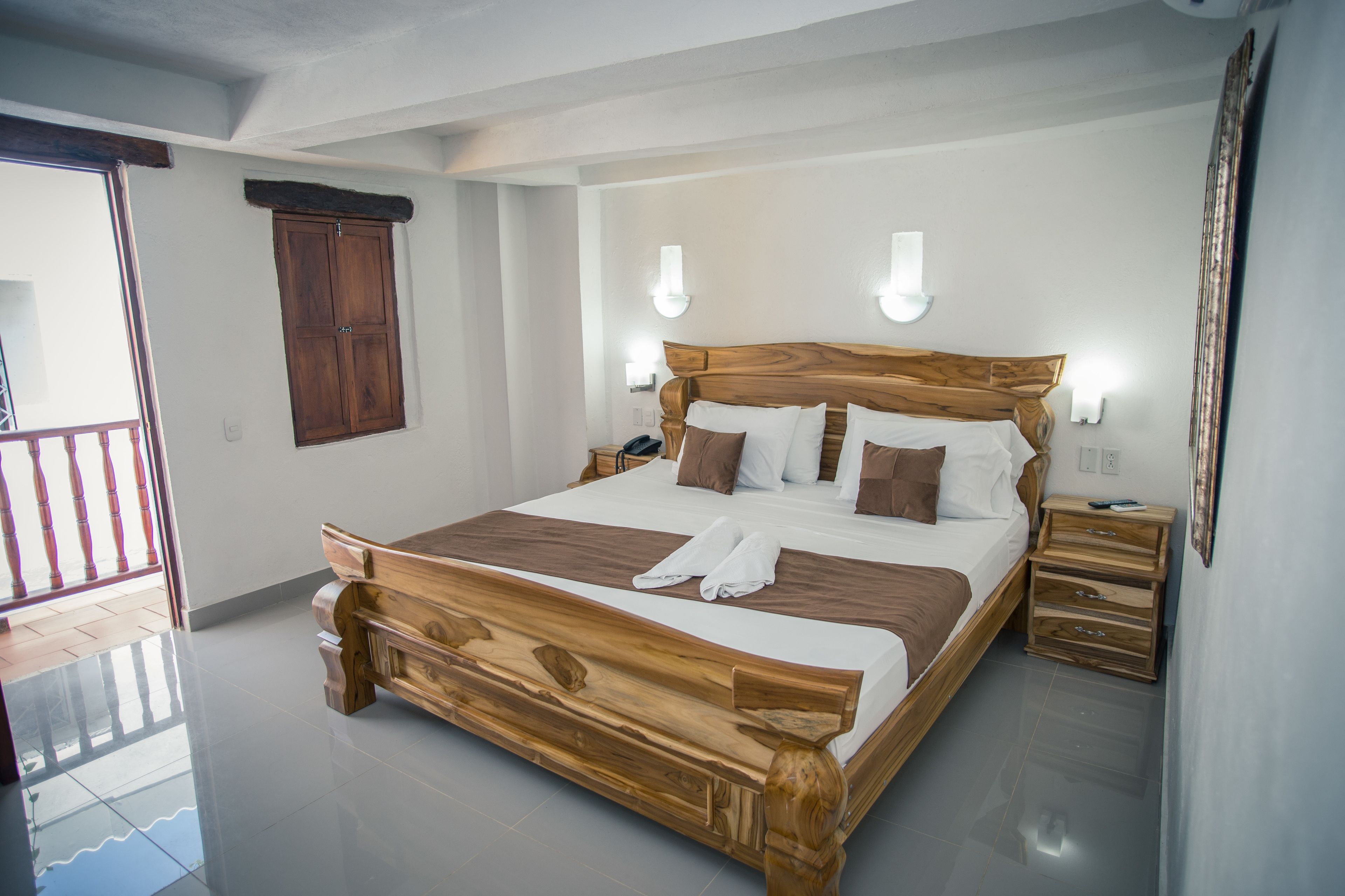 A wooden bed with white and brown bedding, two bedside tables, a wooden wardrobe, and a balcony with a railing.