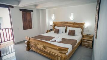 A wooden bed with white and brown bedding, two bedside tables, a wooden wardrobe, and a balcony with a railing.