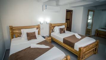 Duas camas de madeira com roupa de cama branca e castanha, uma mesa de cabeceira com telefone e comando, e um ar condicionado fixado na parede.