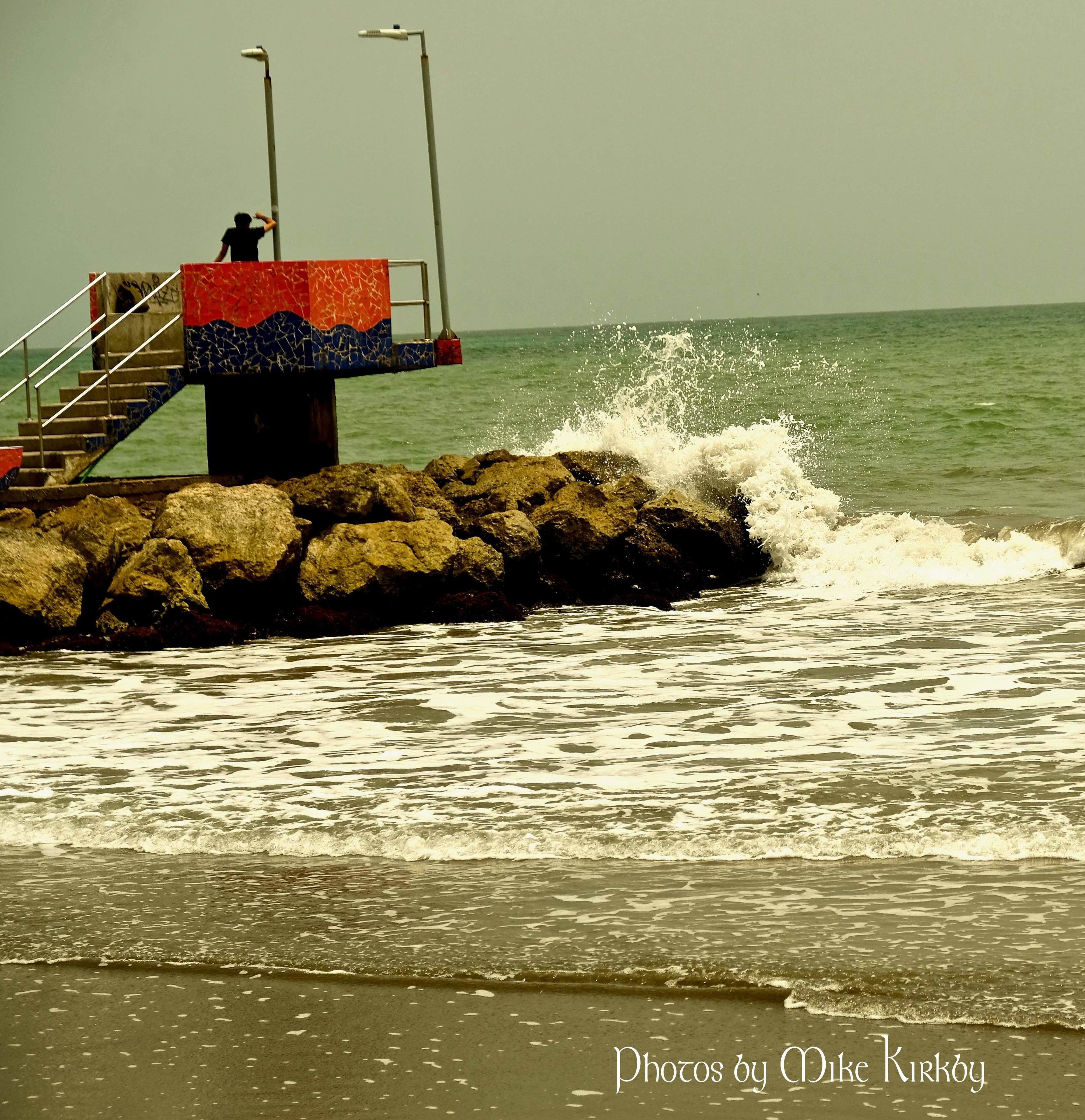 A pier with stairs leading to a platform, a rocky breakwater, and waves crashing against it.
