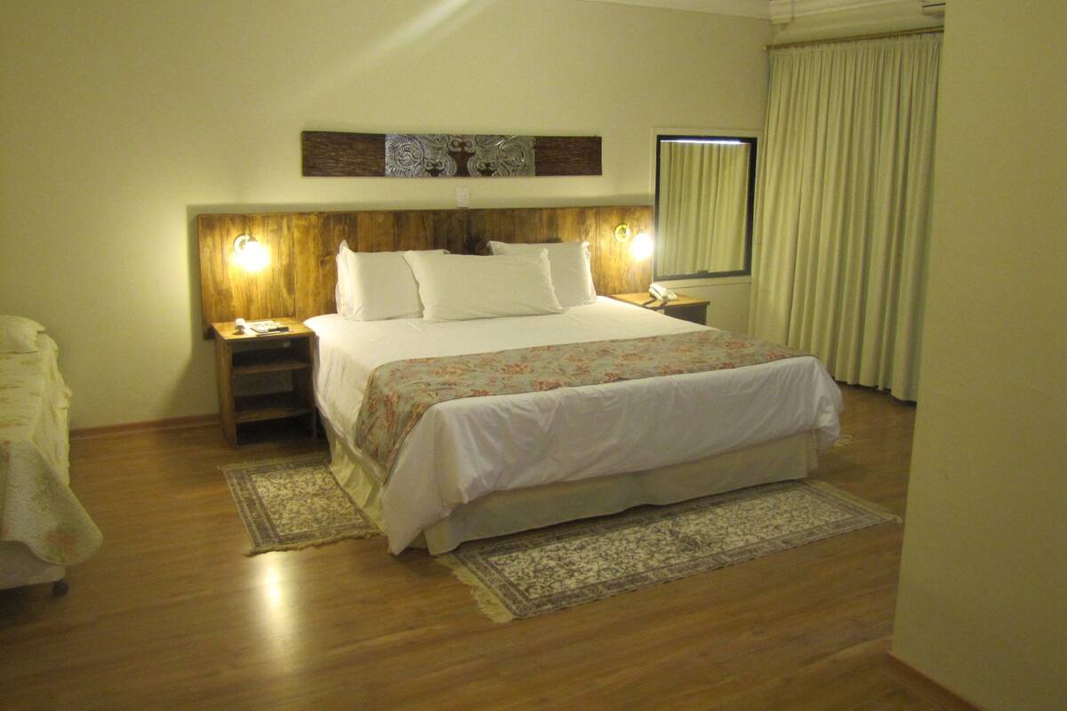 A hotel room with a large bed, wooden headboard, bedside lamps, a nightstand, a telephone, a window with curtains, and a rug.