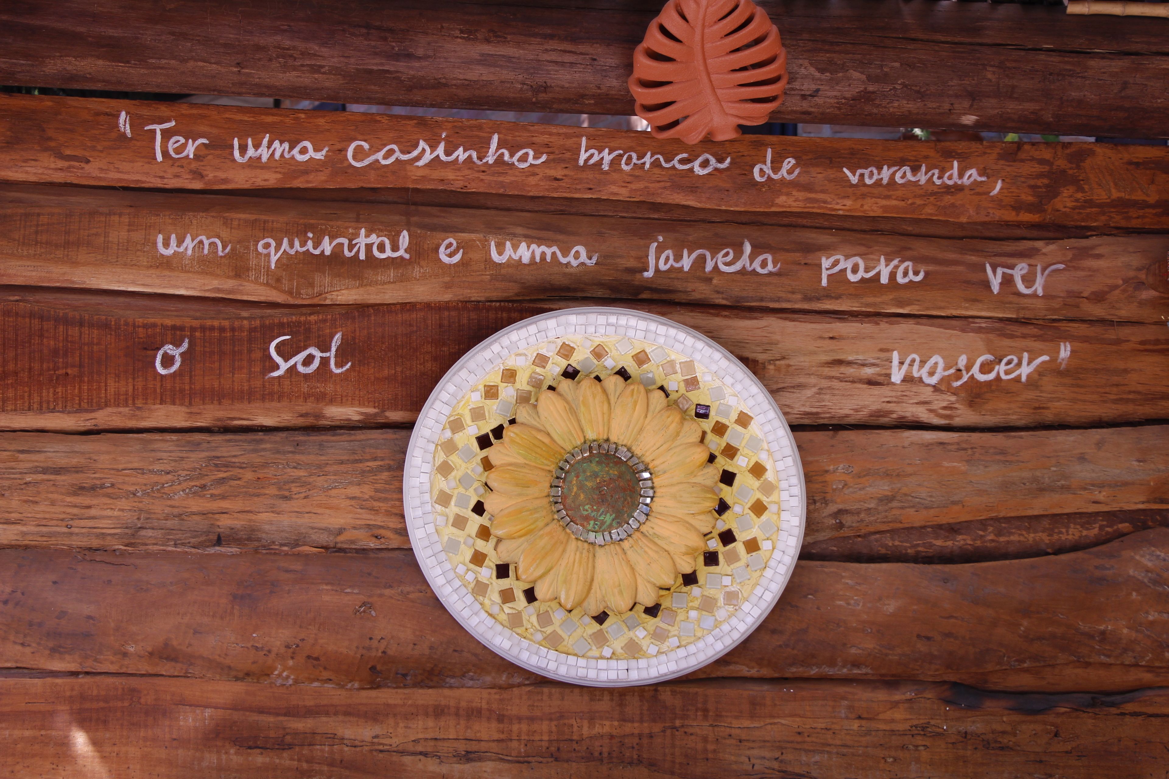 A wooden table with a mosaic sun design and a quote in Portuguese.