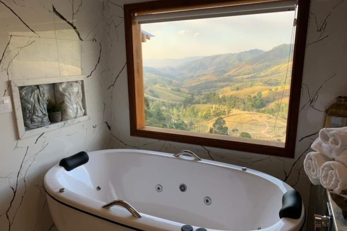 A bathroom with a freestanding bathtub, a window with a view of rolling hills, and a towel rack with folded towels.