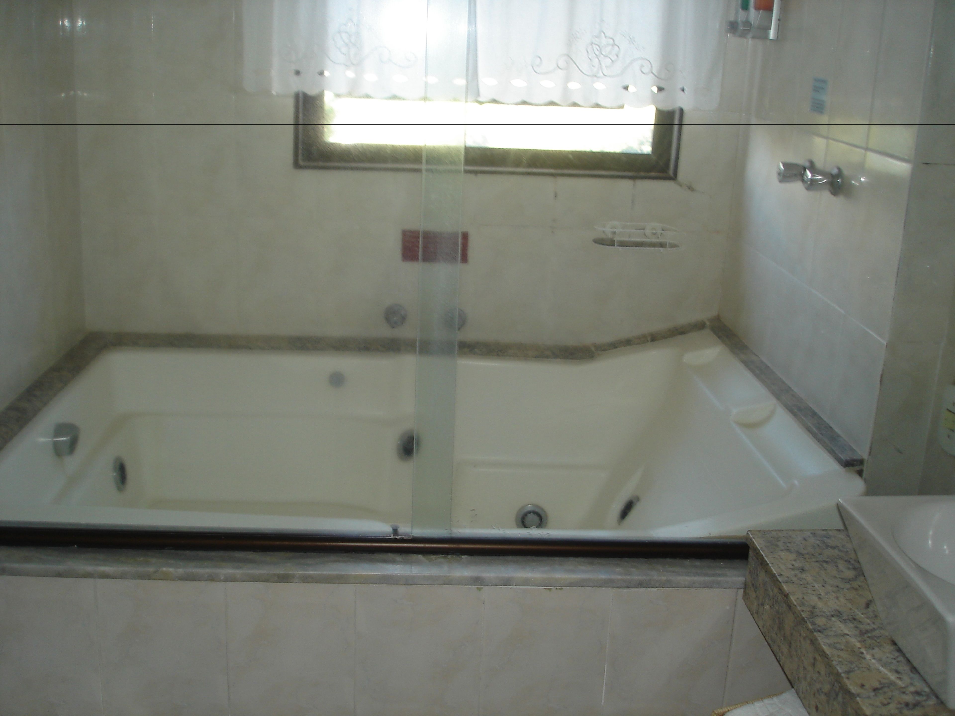 A bathroom with a large bathtub, a window with a curtain, and tiled walls.