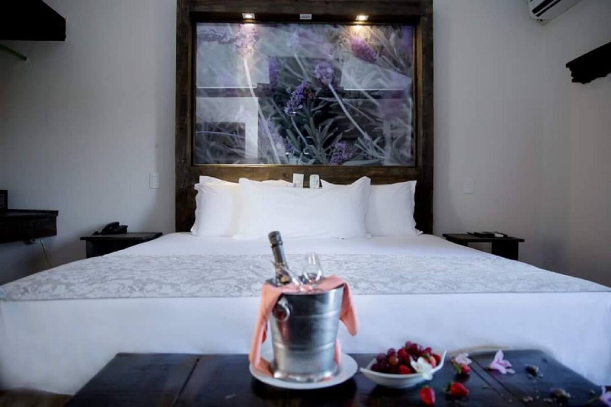 A hotel room with a bed, a bedside table with a bottle of champagne, and a bowl of strawberries.