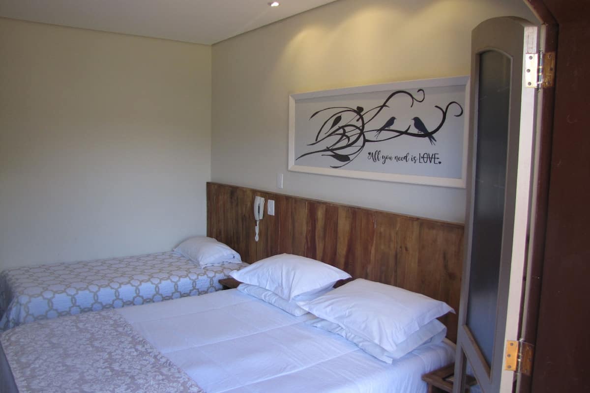 A hotel room with two beds, a wooden headboard, a wall-mounted phone, and a decorative piece with a quote.