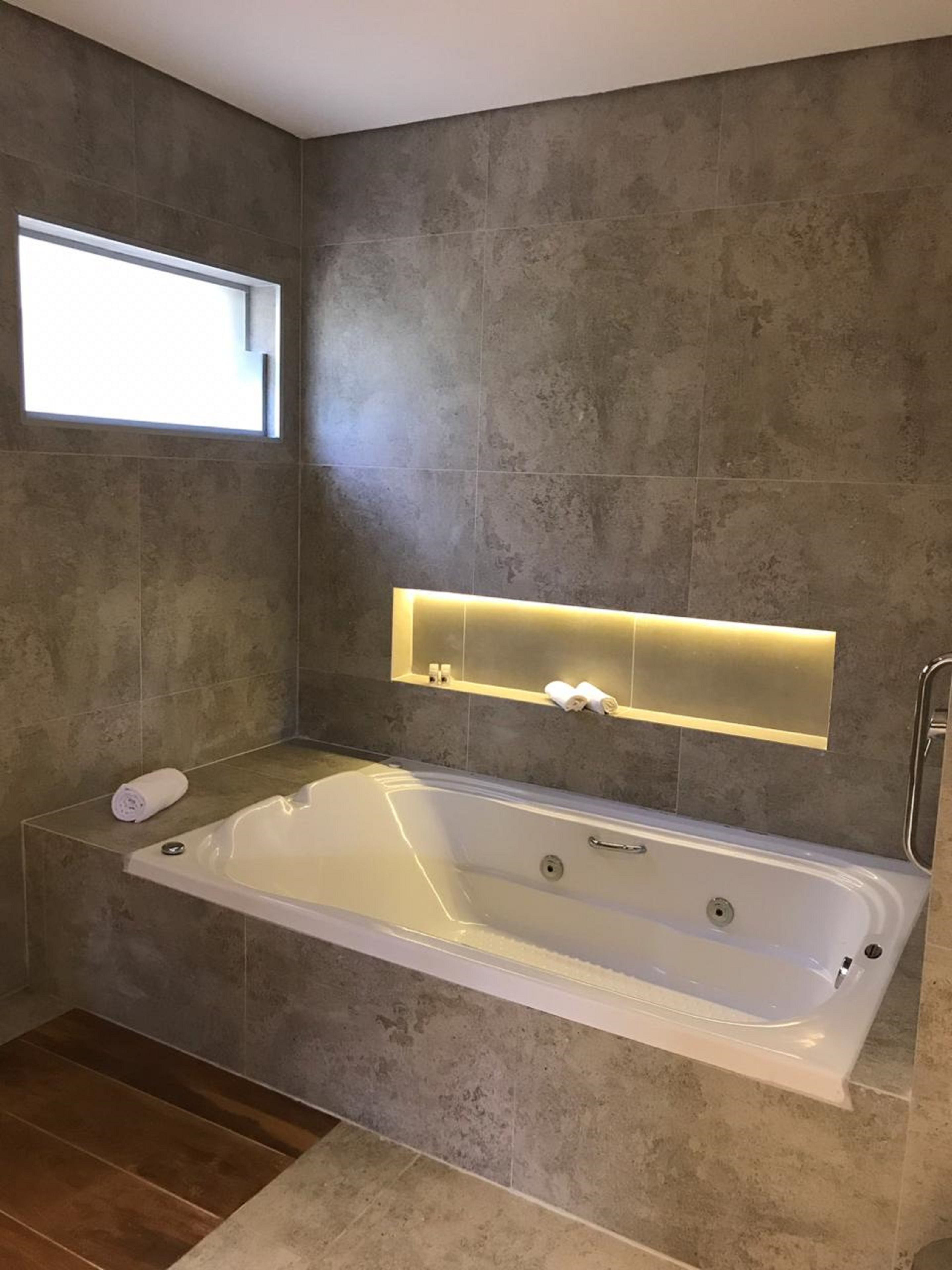 A modern bathroom with a large bathtub, a window, and a built-in shelf with towels.