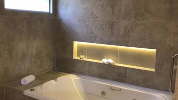 A modern bathroom with a large bathtub, a window, and a built-in shelf with towels.