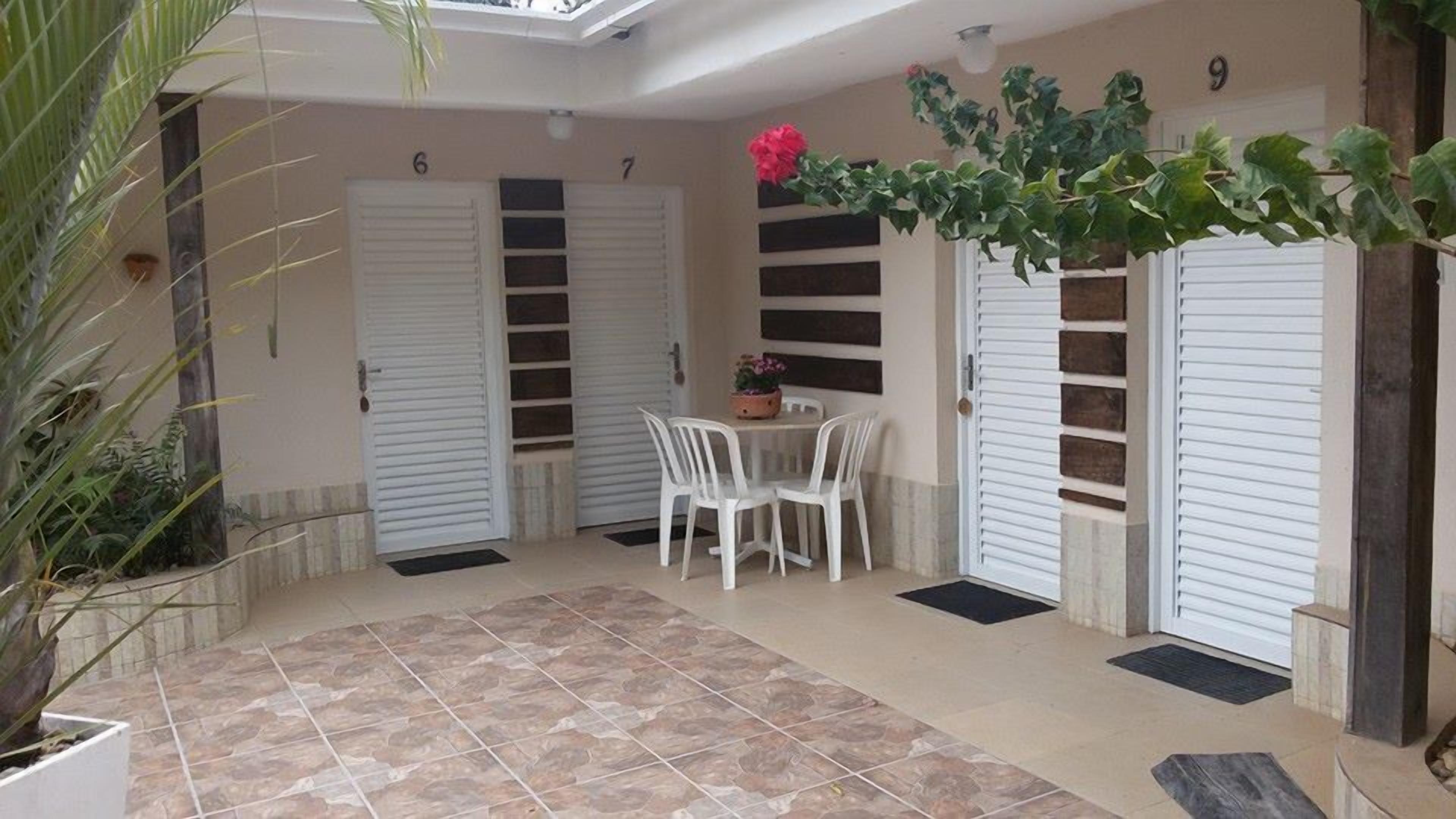 A covered patio with a tiled floor, two white doors, a small table with chairs, and potted plants.