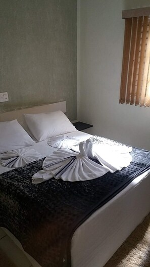 A hotel room with a bed, white pillows, a dark patterned bedspread, and a window with blinds. - Pousada Vale da Serra (Serra Negra)