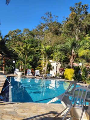 A swimming pool with lounge chairs and tropical vegetation. - Pousada Vale da Serra (Serra Negra)