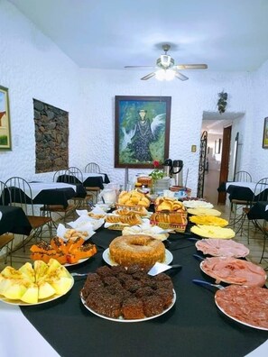 A dining area with a table set for a meal, featuring various dishes and a painting on the wall. - Pousada Vale da Serra (Serra Negra)