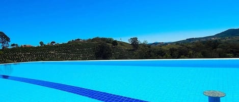 A clear blue swimming pool with a tiled deck, surrounded by a landscaped area with trees and hills in the background.