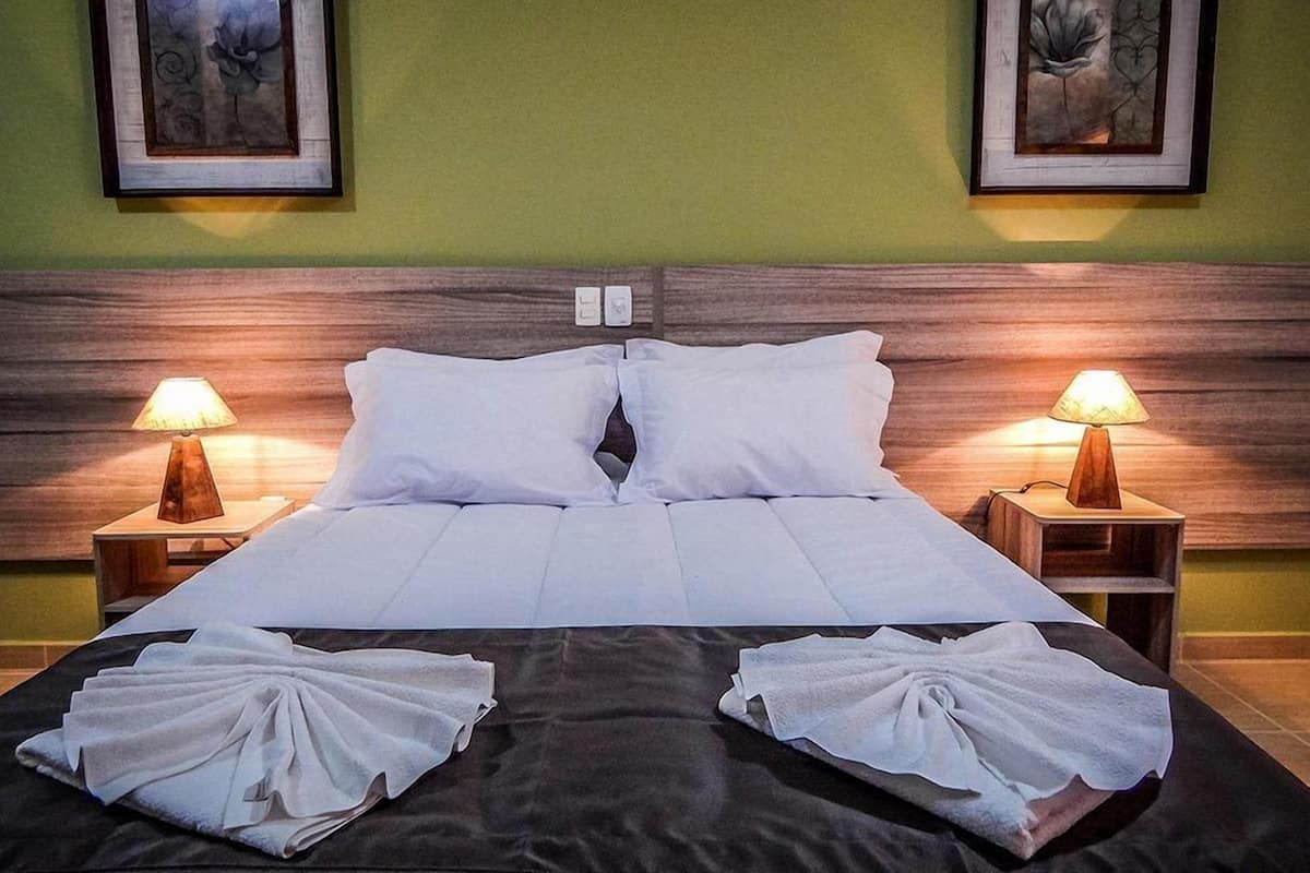 A neatly made bed with white linens, two bedside lamps, and two framed floral artworks on the wall.