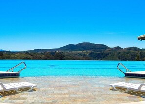 A swimming pool with clear blue water, two white lounge chairs, and a view of a hilly landscape in the background. - Hotel Fazenda Molise (Serra Negra)