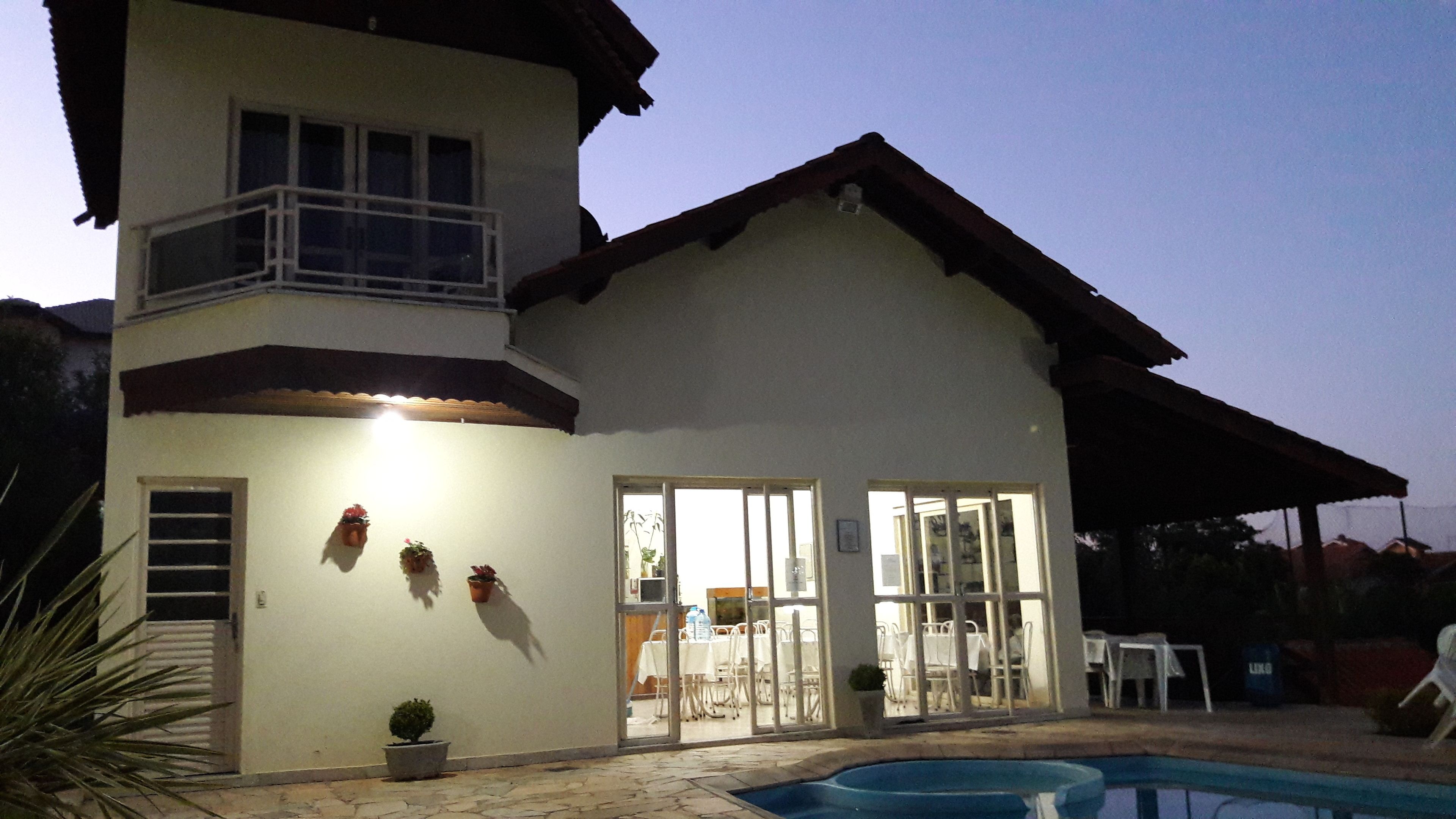 A two-story house with a balcony, a swimming pool, and a dining area with tables and chairs.