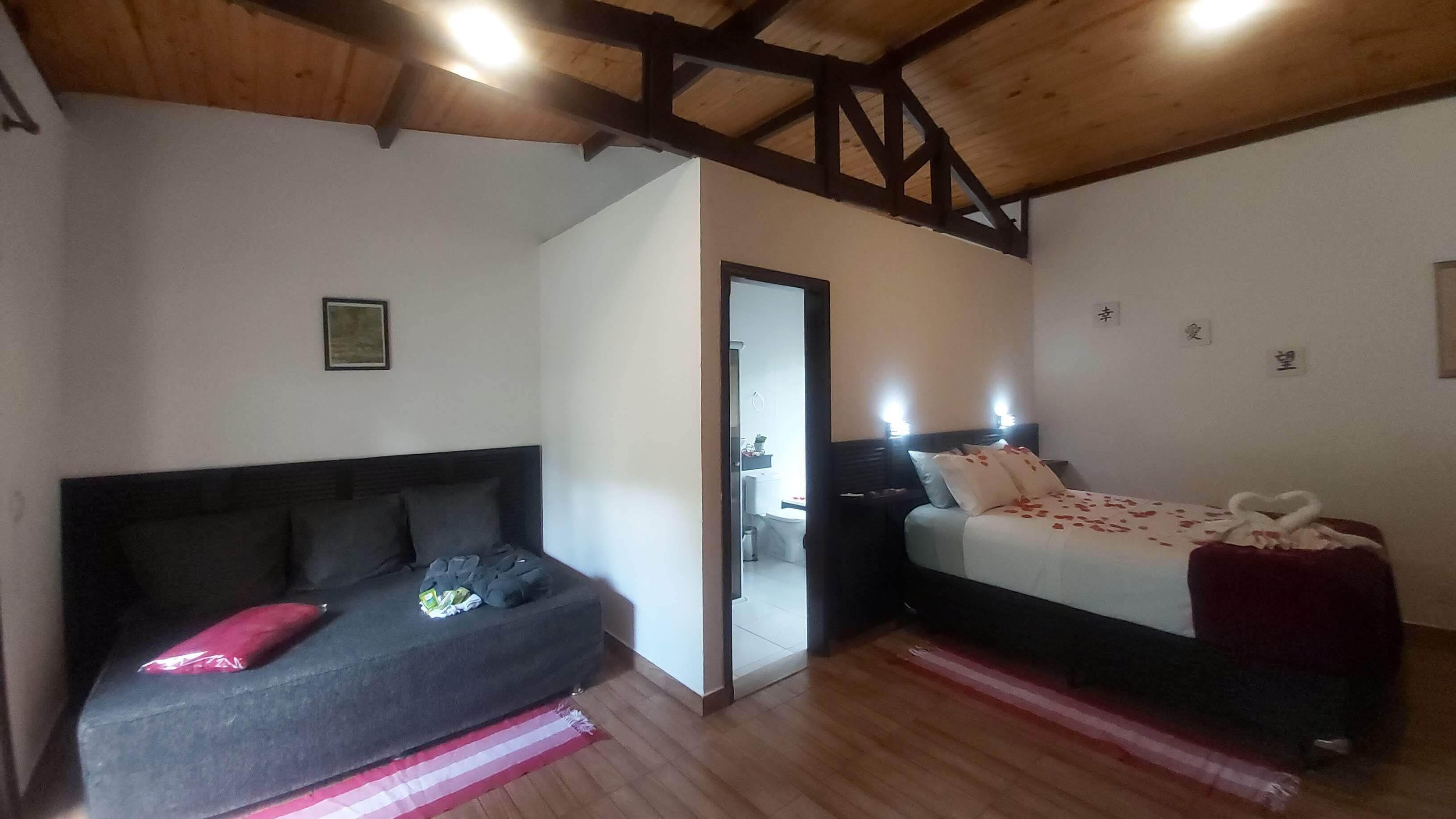 Ein Schlafzimmer mit Bett, einer Couch, einer Holzbalkendecke und einer Tür zu einem Badezimmer.