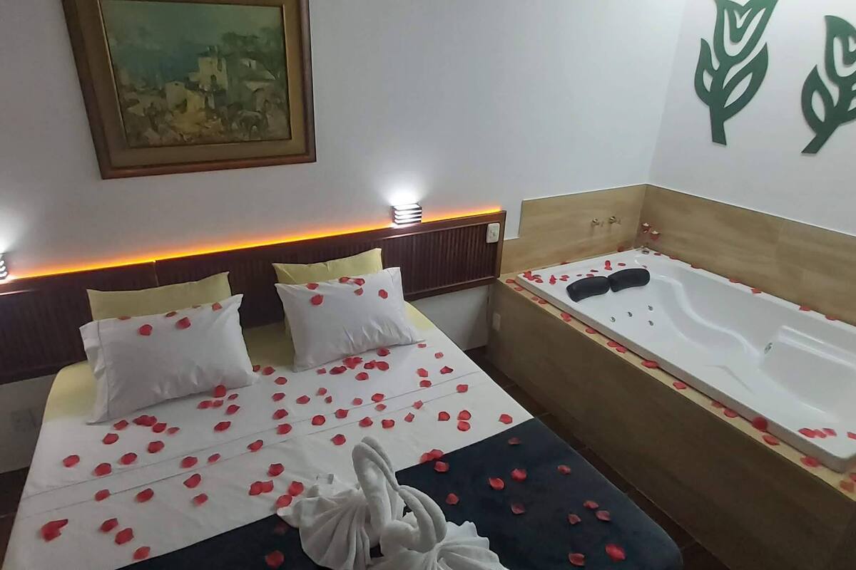 A hotel room with a bed, a bathtub, and a painting on the wall.