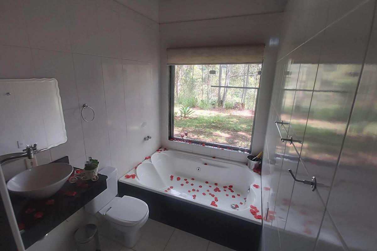 A modern bathroom with a bathtub, toilet, sink, and a window with a view of greenery.