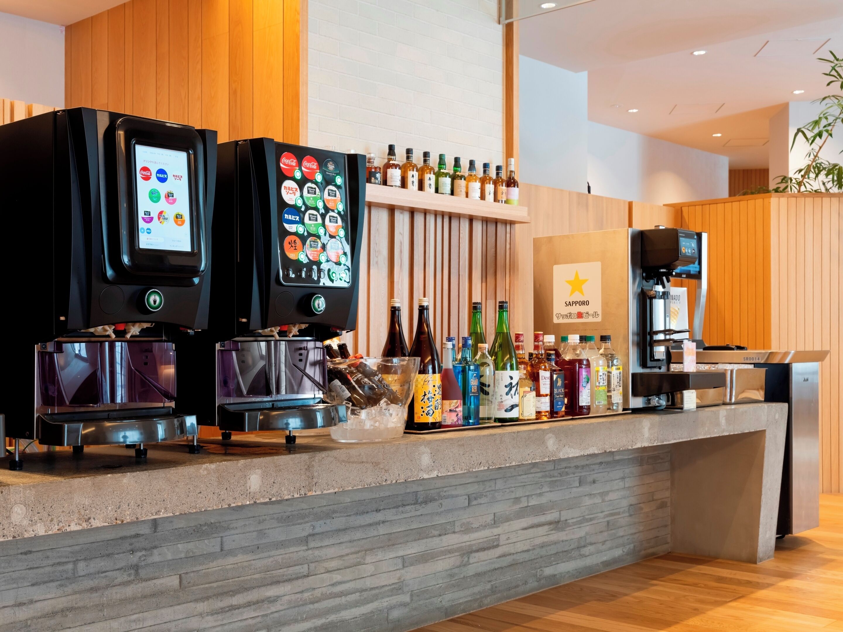 A modern bar area with multiple beverage dispensers, a variety of alcohol bottles, and a branded sign.