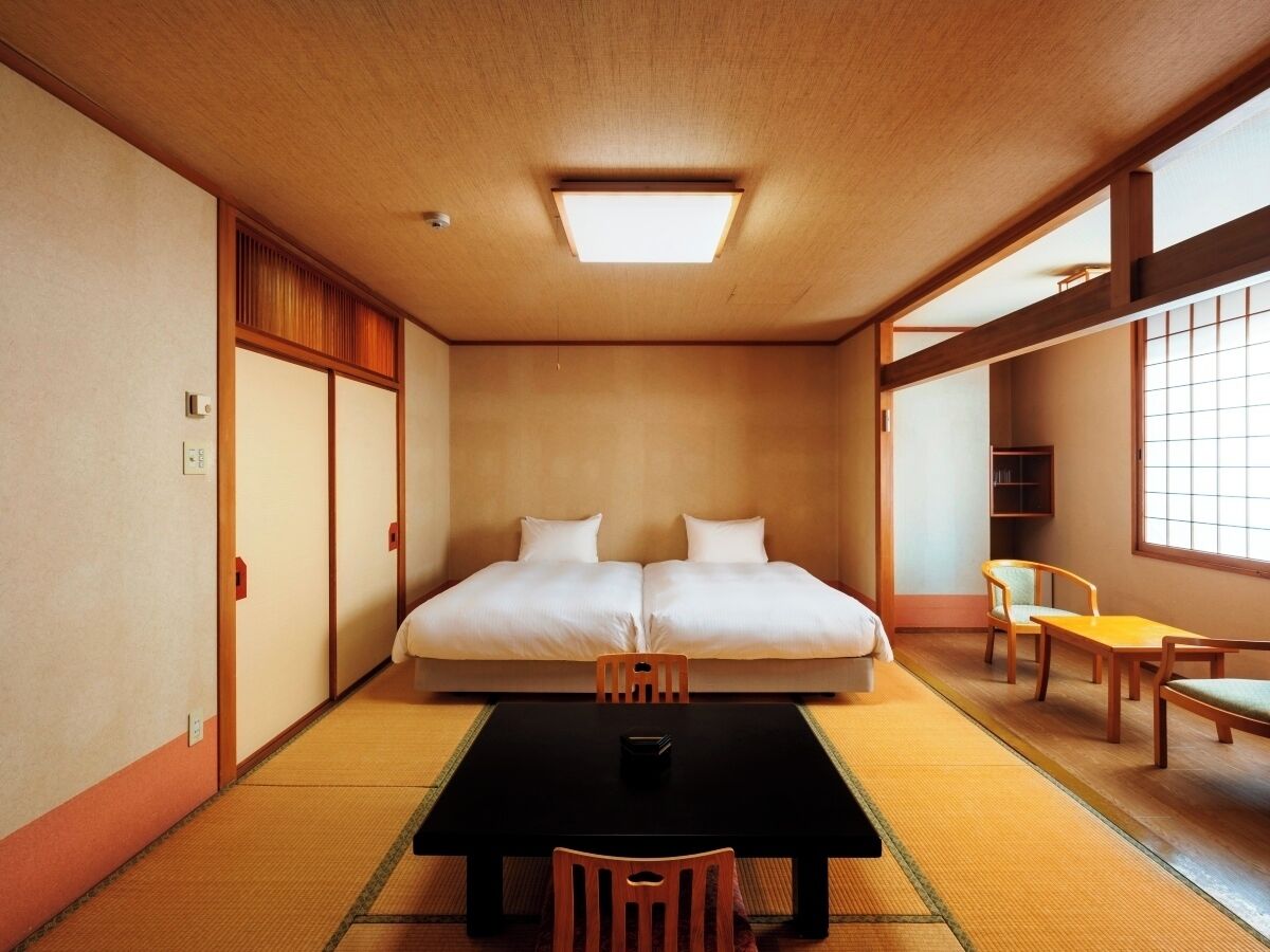 A traditional Japanese room with tatami flooring, a futon bed, a small table, and a window.