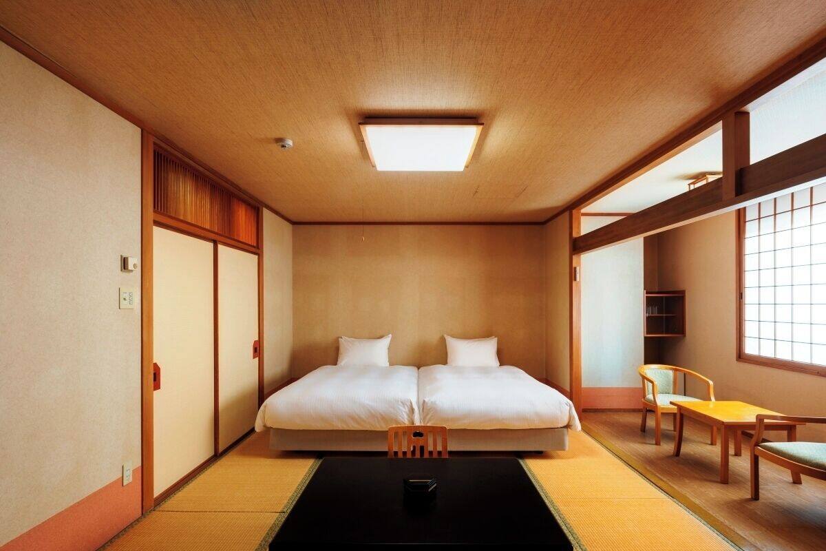 Una habitación japonesa tradicional con suelo de tatami, un futón, una pequeña mesa y una ventana.