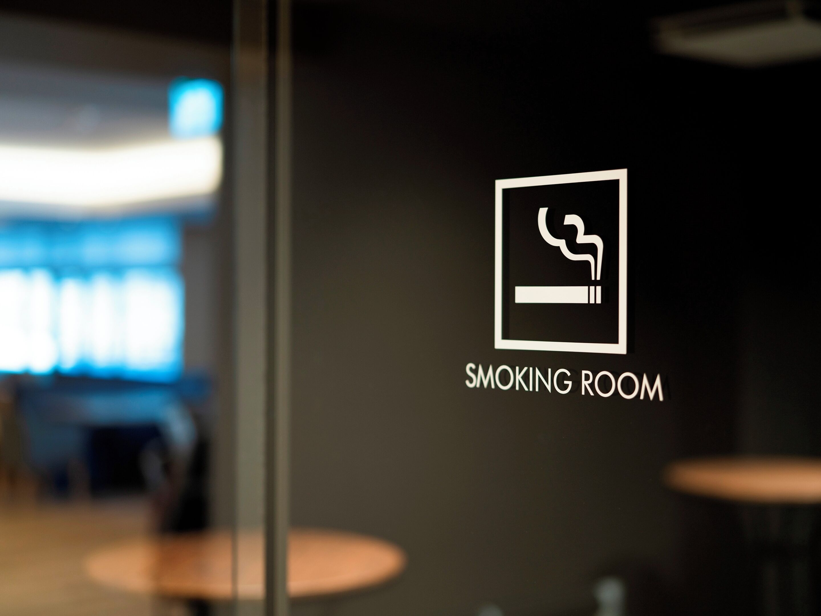 Señal que indica una sala para fumadores, con el icono de un cigarrillo y la inscripción 'SMOKING ROOM' sobre un fondo oscuro.