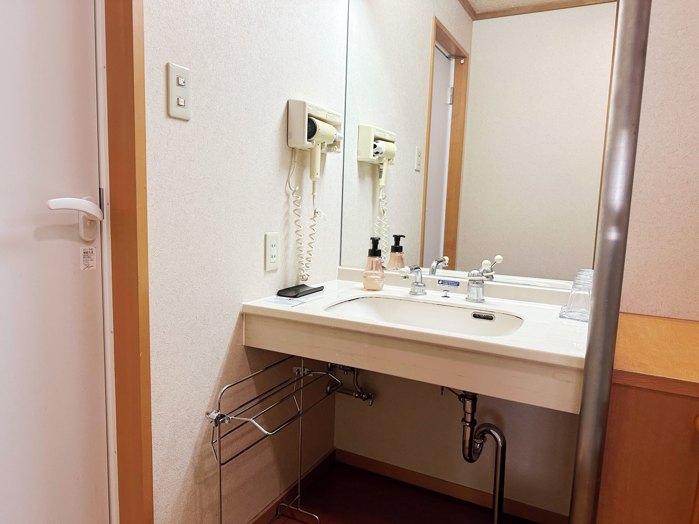 Een badkamer met een wastafel, spiegel en een aan de muur bevestigde haardroger.