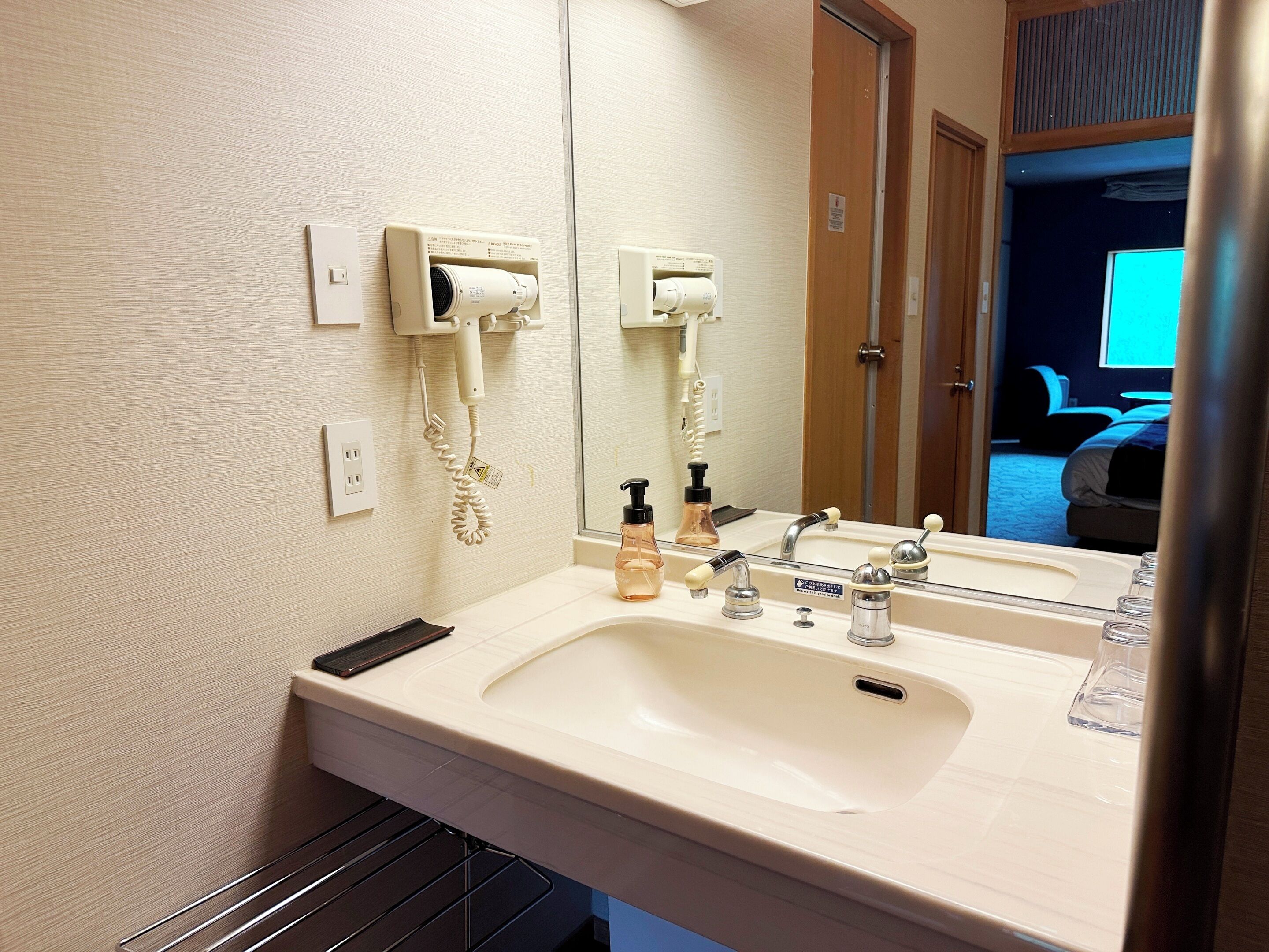 Une salle de bain d’hôtel équipée d’un lavabo, d’un miroir et d’un sèche-cheveux.