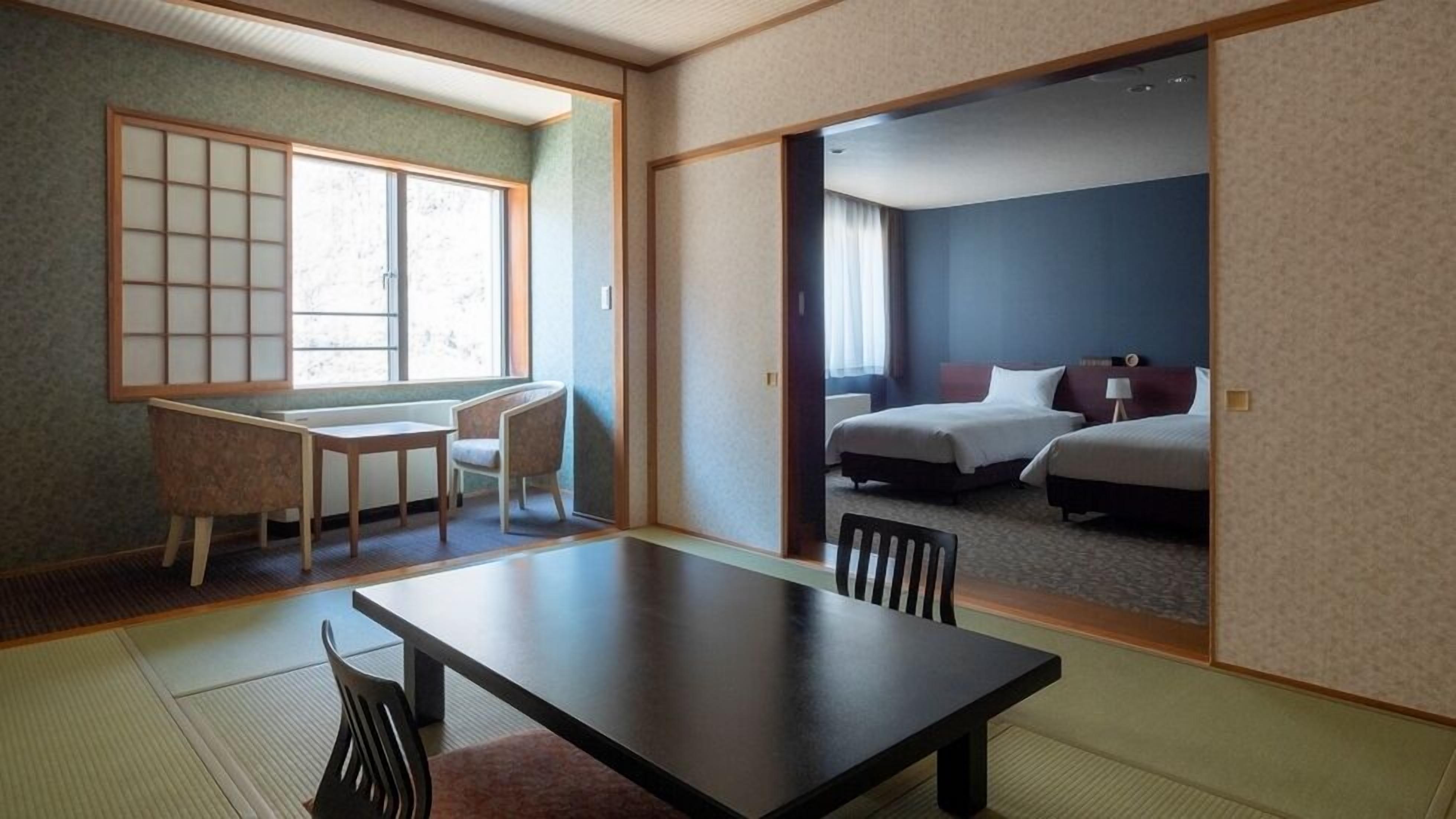 A traditional Japanese-style room with tatami flooring, a low table, and a sliding door leading to a bedroom with two beds.