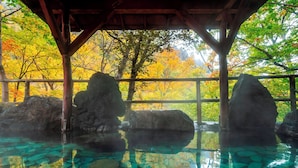 A clear pool with rocks and a wooden structure with a view of autumn trees. - Sounkaku  (Kamikawa)