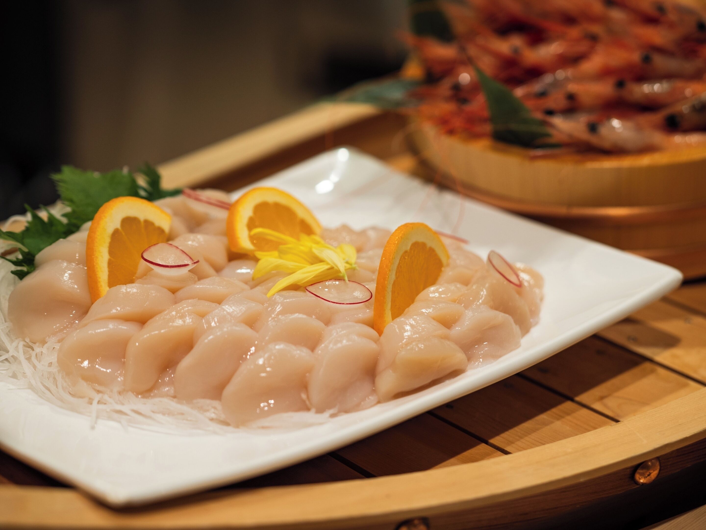 A plate of sashimi with orange slices and radish on a white plate.