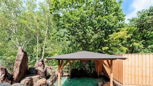 A wooden structure with a roof, surrounded by large rocks and a clear water feature. - Sounkaku  (Kamikawa)
