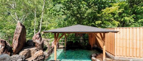 A wooden structure with a roof, surrounded by large rocks and a clear water feature.