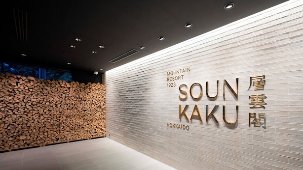 A reception area with a wall-mounted sign for Mountain Resort 1923, and a stack of firewood against the wall. - Sounkaku  (Kamikawa)