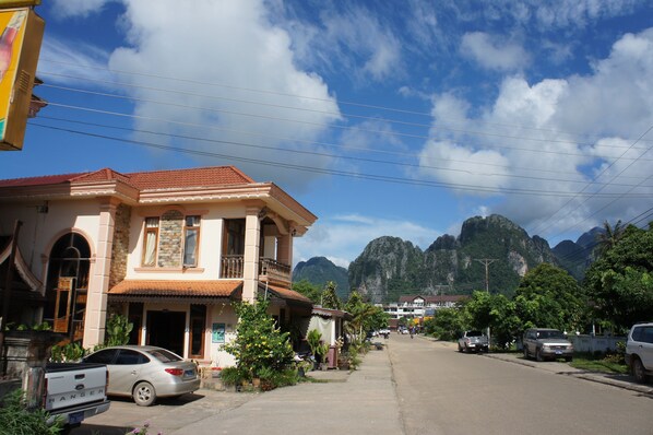 A two-story building with a balcony, parked cars, and mountains in the background.