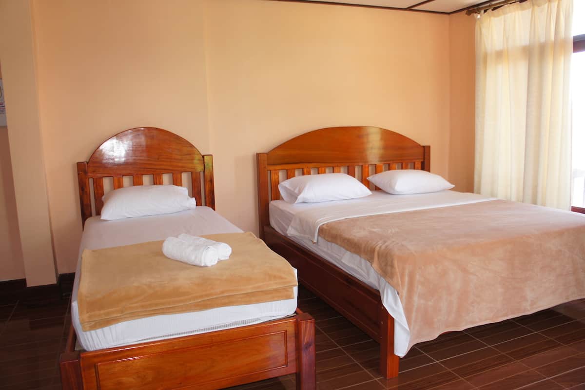Two wooden beds with white linens and beige blankets, in a room with plain walls and a tiled floor.