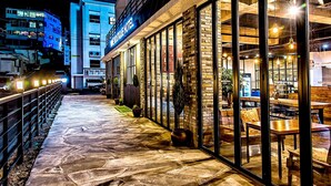 Un hotel con fachada de vidrio, mobiliario exterior y un camino empedrado de piedra.