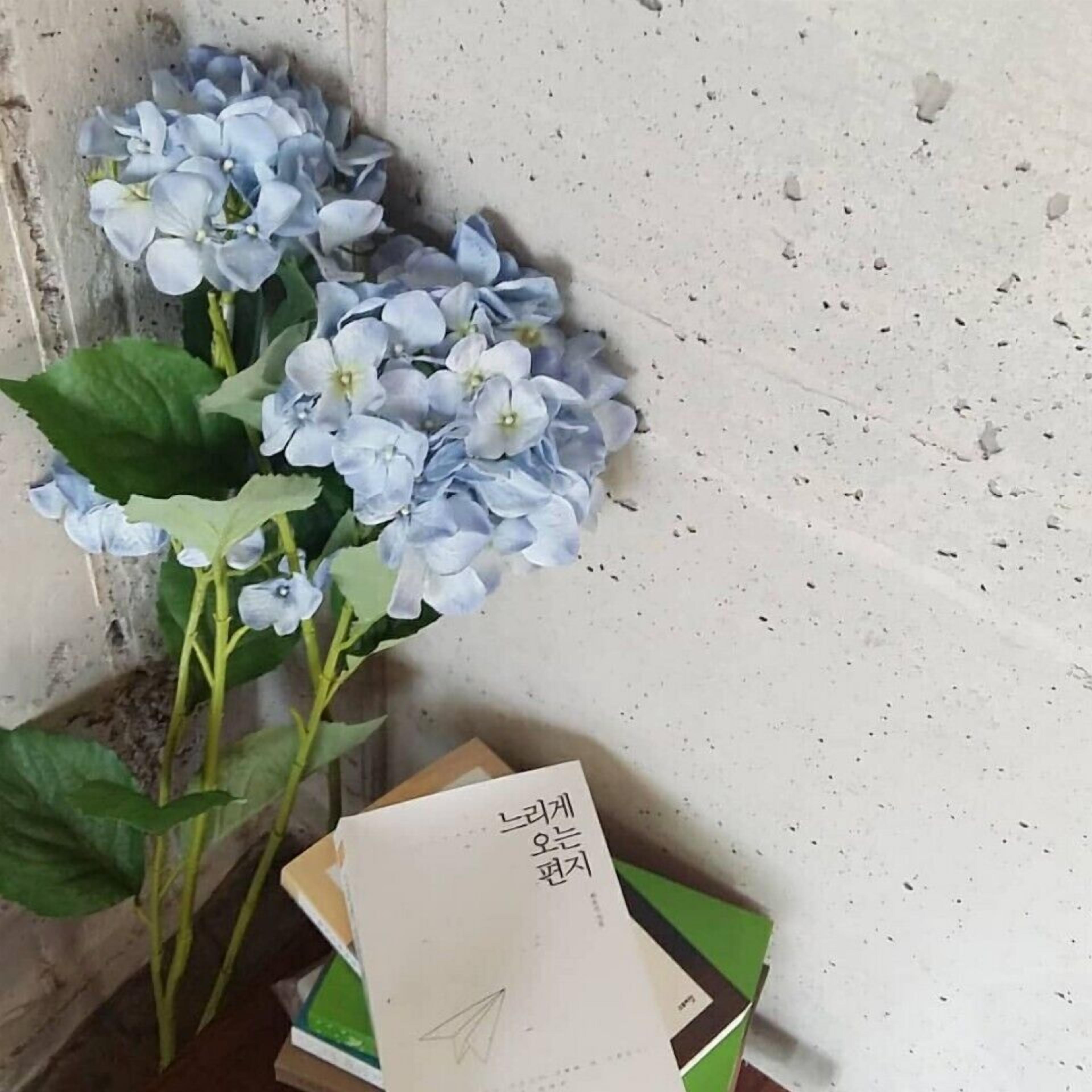 En bukett med blå blommor bredvid en hög med böcker och ett papper med koreansk text.
