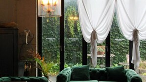 Una habitación acogedora con un sofá verde, una lámpara colgante y vistas al verdor por la ventana.